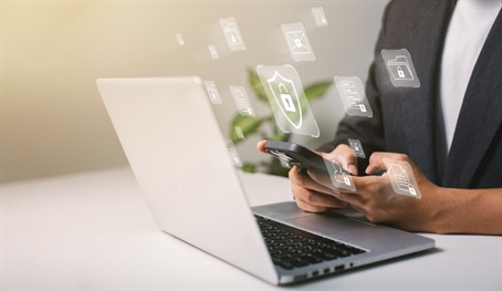 Persona con el celular en la mano, frente a un computador